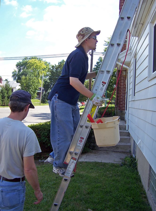 young man climbing ladder to clean gutters